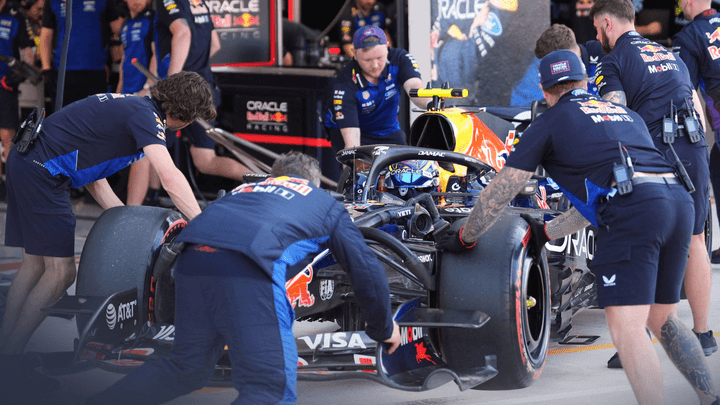 Mécaniciens en combinaison bleue travaillant sur une monoplace de F1 dans les stands lors d'un arrêt au stand